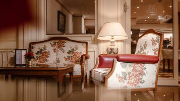 Una habitación luminosa y elegante con piso pulido, un sofá tapizado con motivos florales, un sillón a juego, una mesa con un florero y una lámpara.