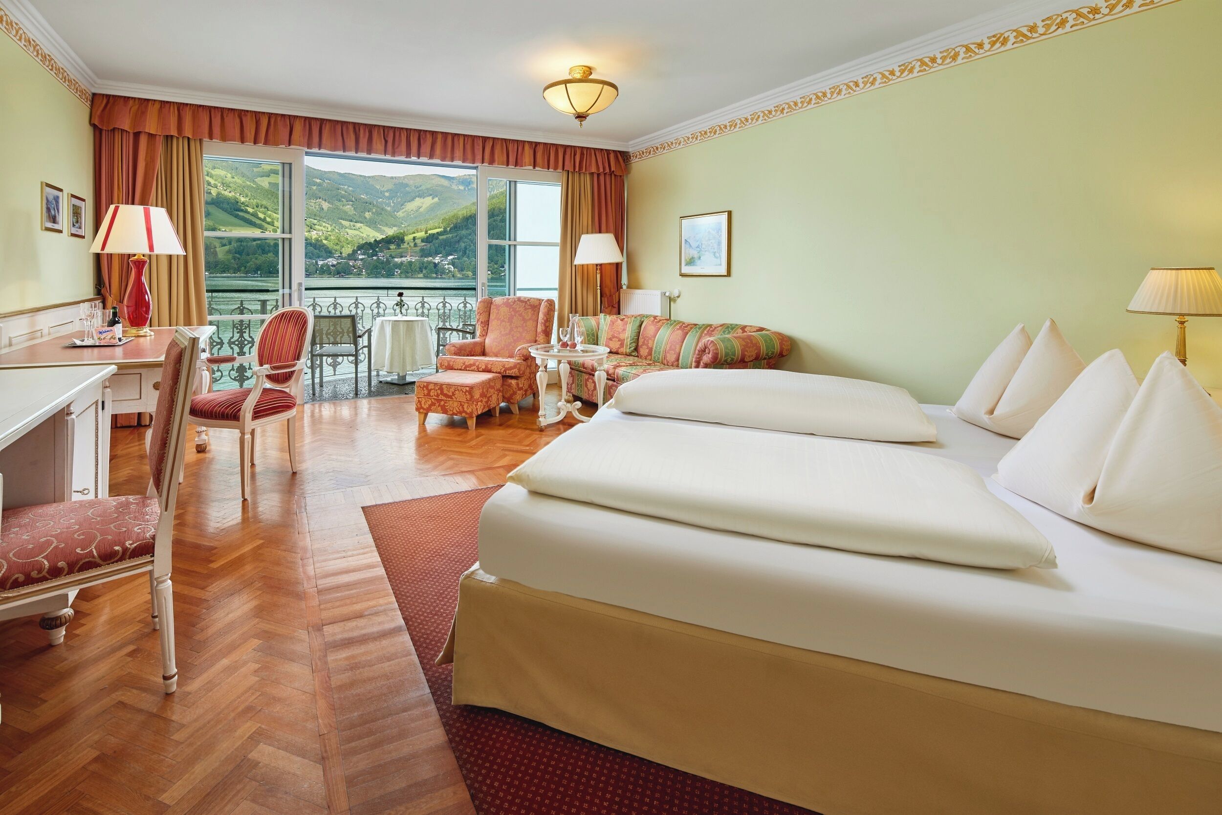 Een hotelkamer met een groot bed, een bureau, een stoel, een bank en een balkon met uitzicht op de bergen.