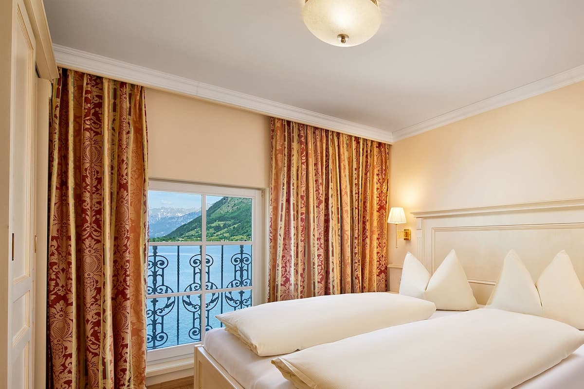 Une chambre d’hôtel avec un lit, des rideaux, une fenêtre donnant sur les montagnes et un luminaire au plafond.