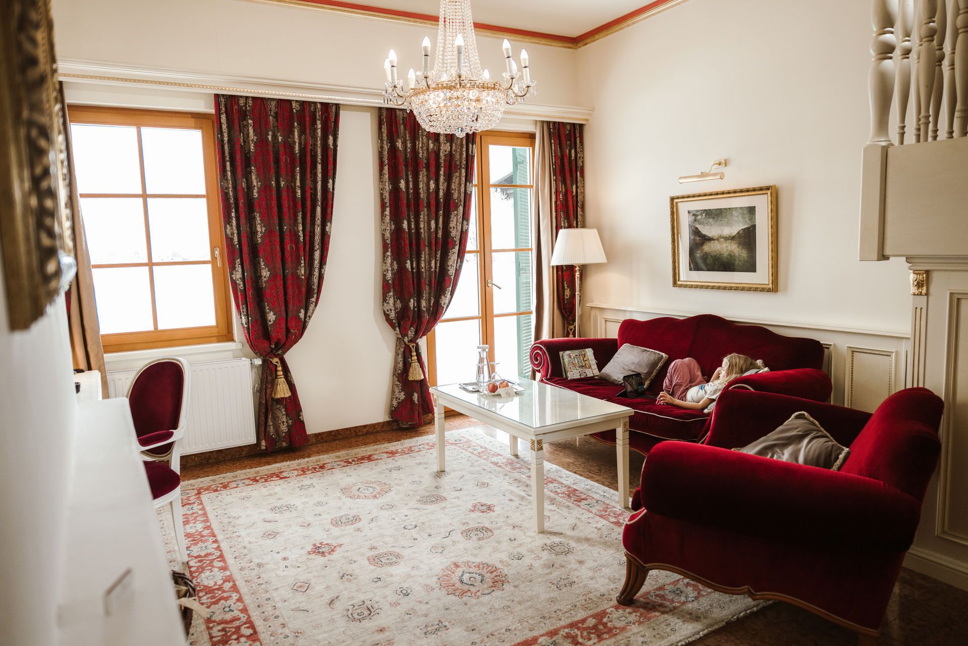 A room with a red sofa, a white coffee table, and a chandelier.