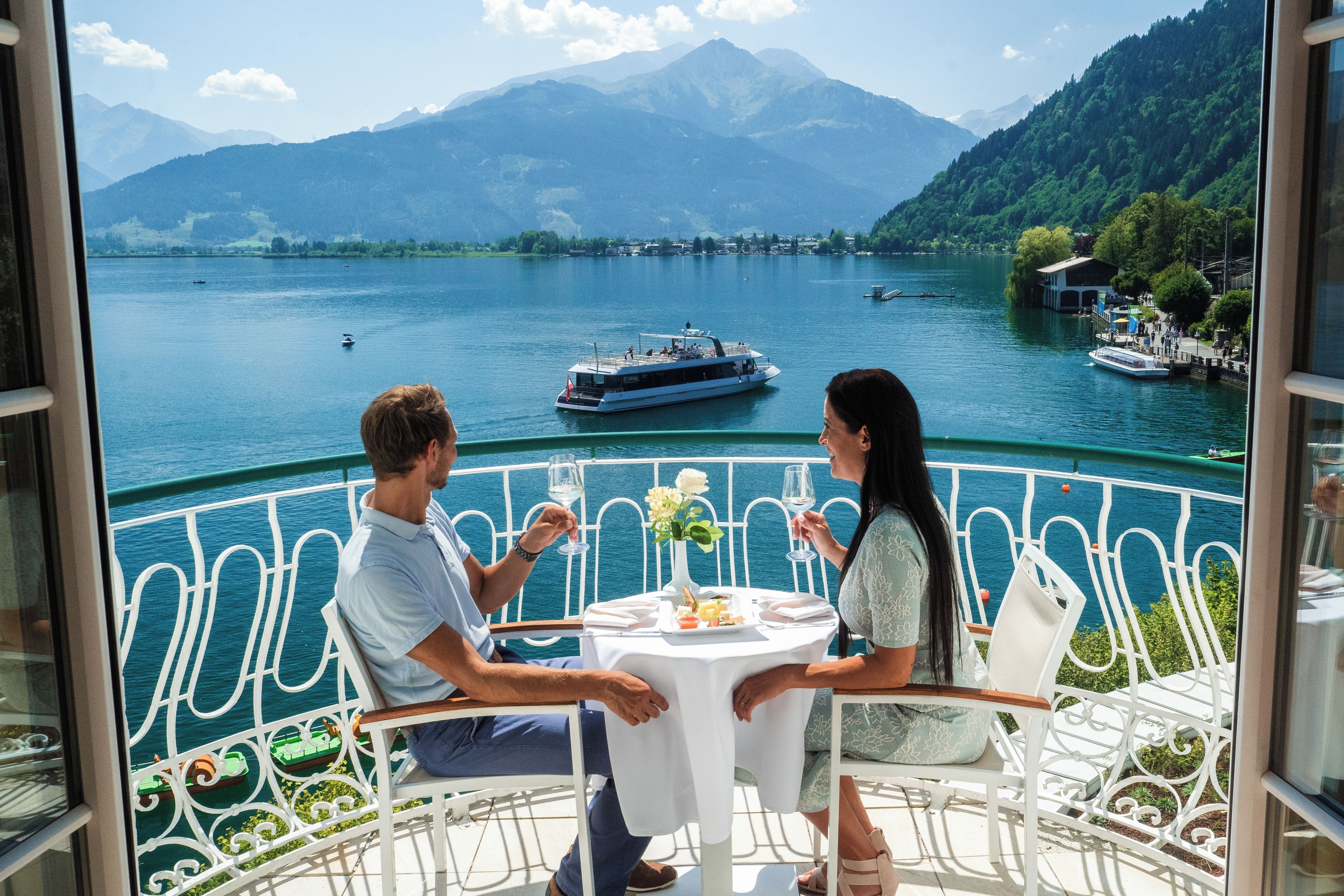 Una pareja cenando en una mesa con vista a un lago y barcos.