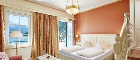 A hotel room with a bed, a small table with a lamp, a view of mountains through the window, and a staircase.