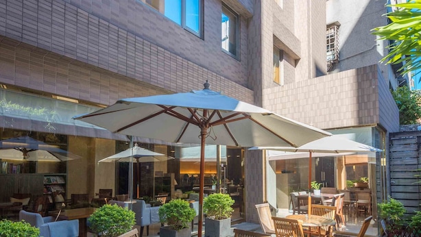 An outdoor patio with wooden tables and chairs, surrounded by potted plants and umbrellas. - Royal Biz Taipei (Taipei)