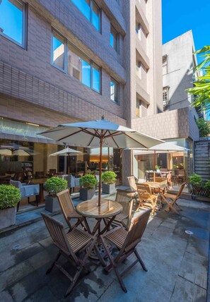 An outdoor patio with wooden tables and chairs, surrounded by potted plants and umbrellas. - Royal Biz Taipei (Taipei)