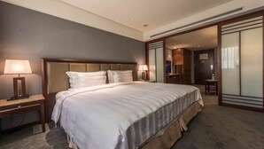 A hotel room with a large bed, two bedside tables with lamps, a wooden headboard, and a view of a hallway with a door. - Royal Biz Taipei (Taipei)