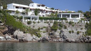 Una propiedad costera con un muro de contención de piedra, un edificio blanco con varios balcones y una vista despejada del mar.