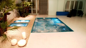 Un área de spa con un jacuzzi, plantas de palma y velas.