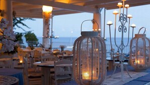 Un área de comedor al aire libre con mesas y sillas, faroles decorativos y vista al mar.