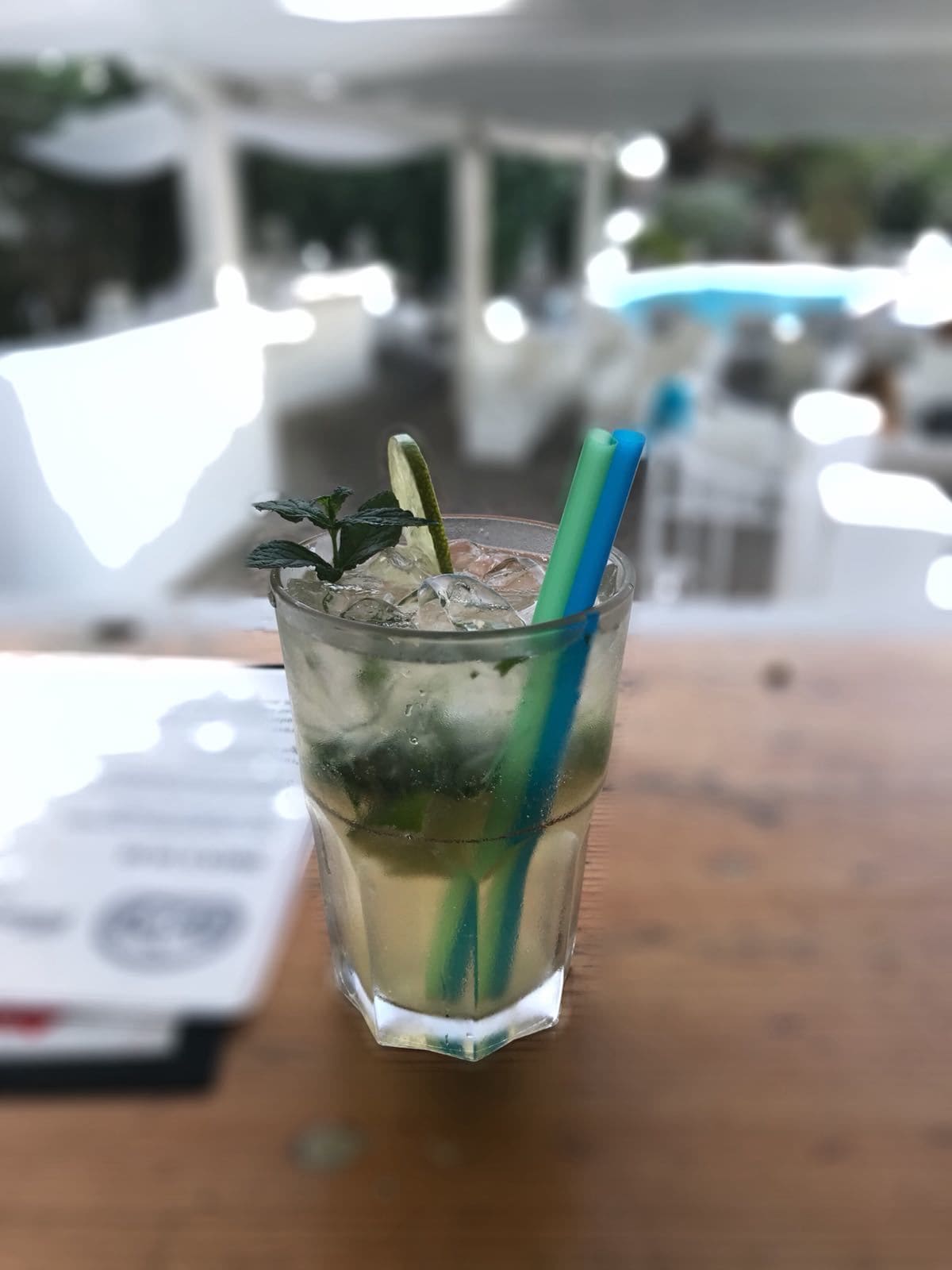 A glass of iced beverage with mint leaves and a lime wedge, placed on a wooden table.