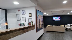 A reception area with a wooden counter, framed certificates, a clock, and a television displaying 'BELLA TURA'. - S.J. Suites Hotel (San Juan)