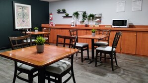 A dining area with wooden tables and chairs, a microwave on the counter, and potted plants. - S.J. Suites Hotel (San Juan)
