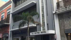A modern hotel with a sign reading "S.J. Suites Hotel". There are cars parked in front, and a palm tree in a planter. - S.J. Suites Hotel (San Juan)