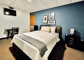 Habitación de hotel con cama, escritorio, silla, televisor montado en la pared y cuadros en la pared.