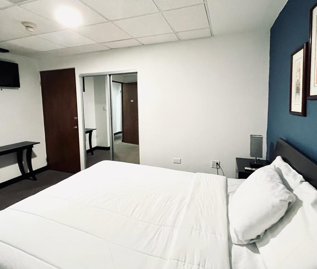 A hotel room with a bed, a desk, a chair, a TV, and a door leading to another room.