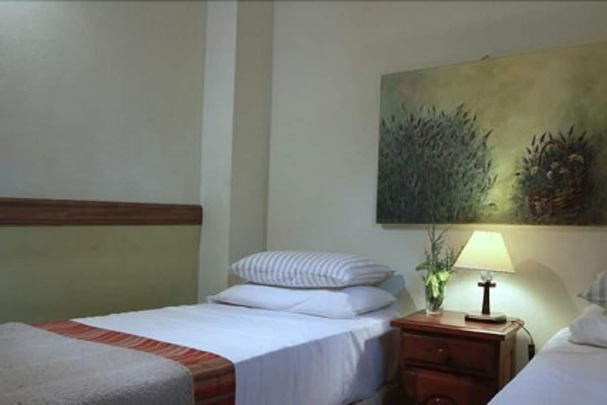Ein Hotelzimmer mit zwei Einzelbetten, einem Nachttisch mit Lampe und einem Bild an der Wand.