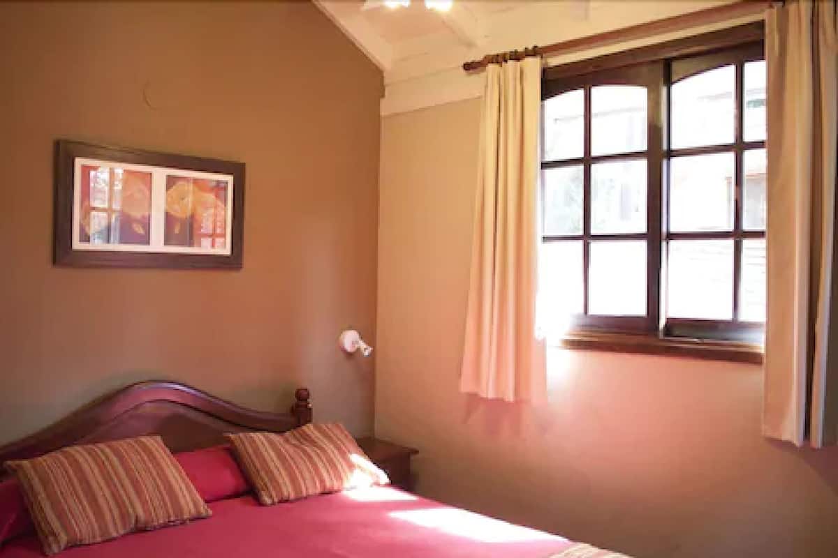 Ein Schlafzimmer mit einem hölzernen Bett, einem Fenster mit Vorhängen und einem gerahmten Bild an der Wand.
