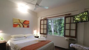 Ein Schlafzimmer mit Bett, Deckenventilator, Fenster mit Vorhängen und einem Gemälde an der Wand.