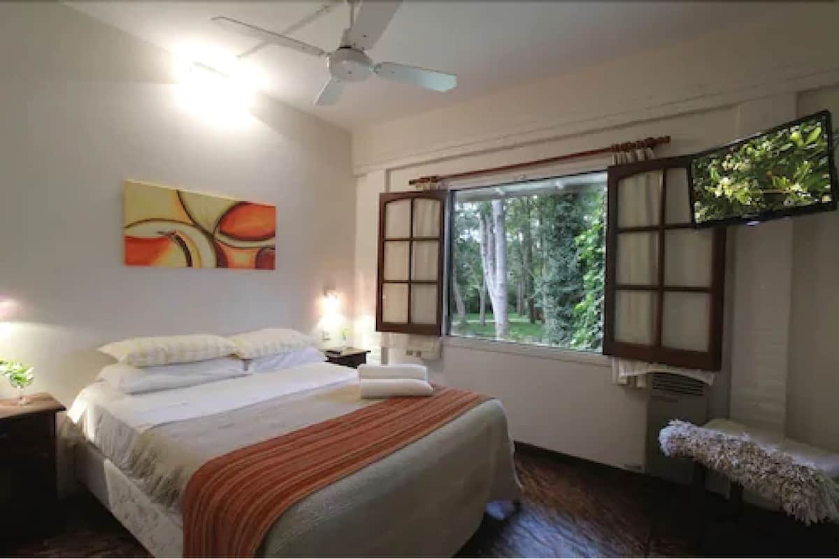 Ein Schlafzimmer mit Bett, Deckenventilator, Fenster mit Vorhängen und einem Gemälde an der Wand.
