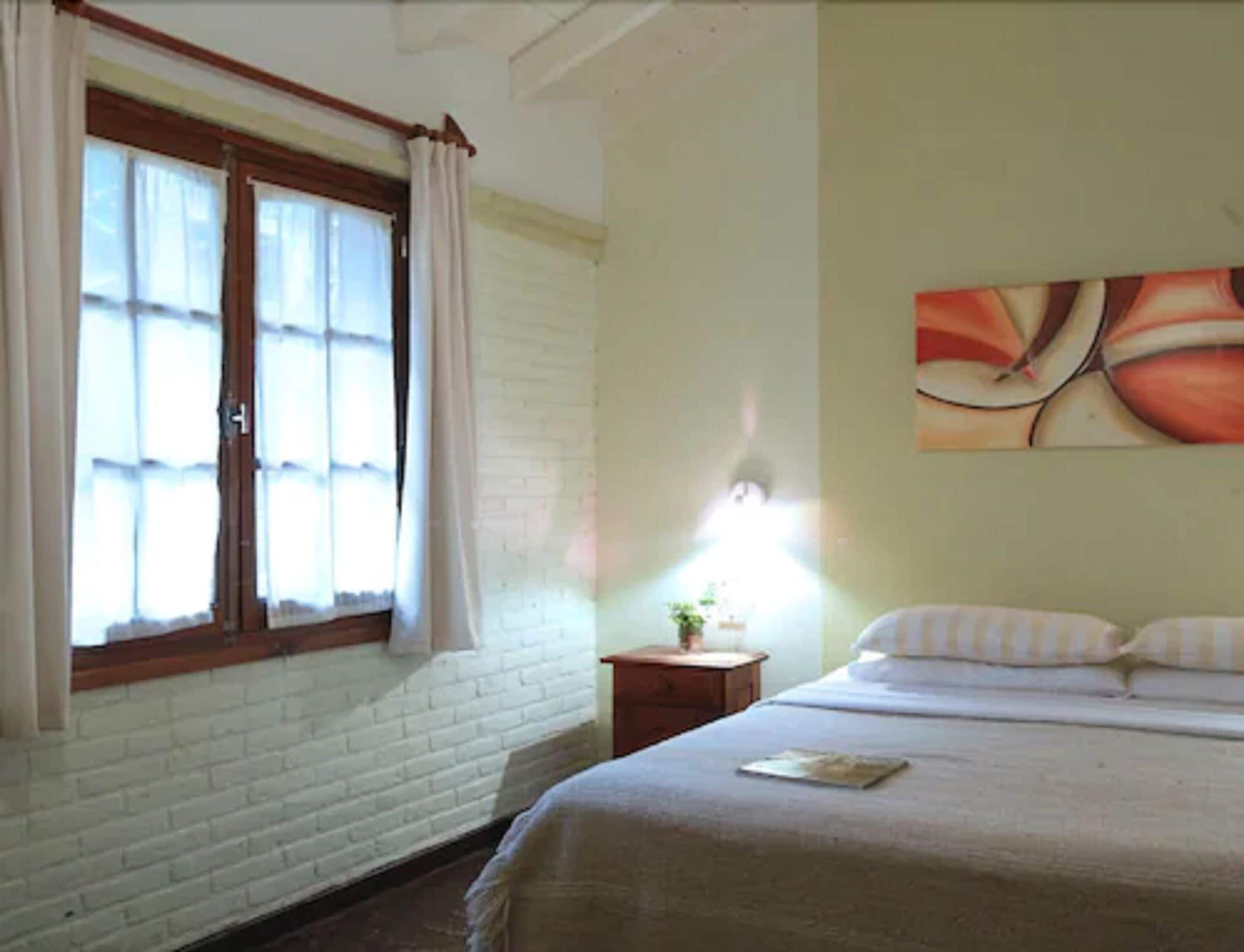 A bedroom with a bed, a nightstand, a lamp, and a window with curtains.