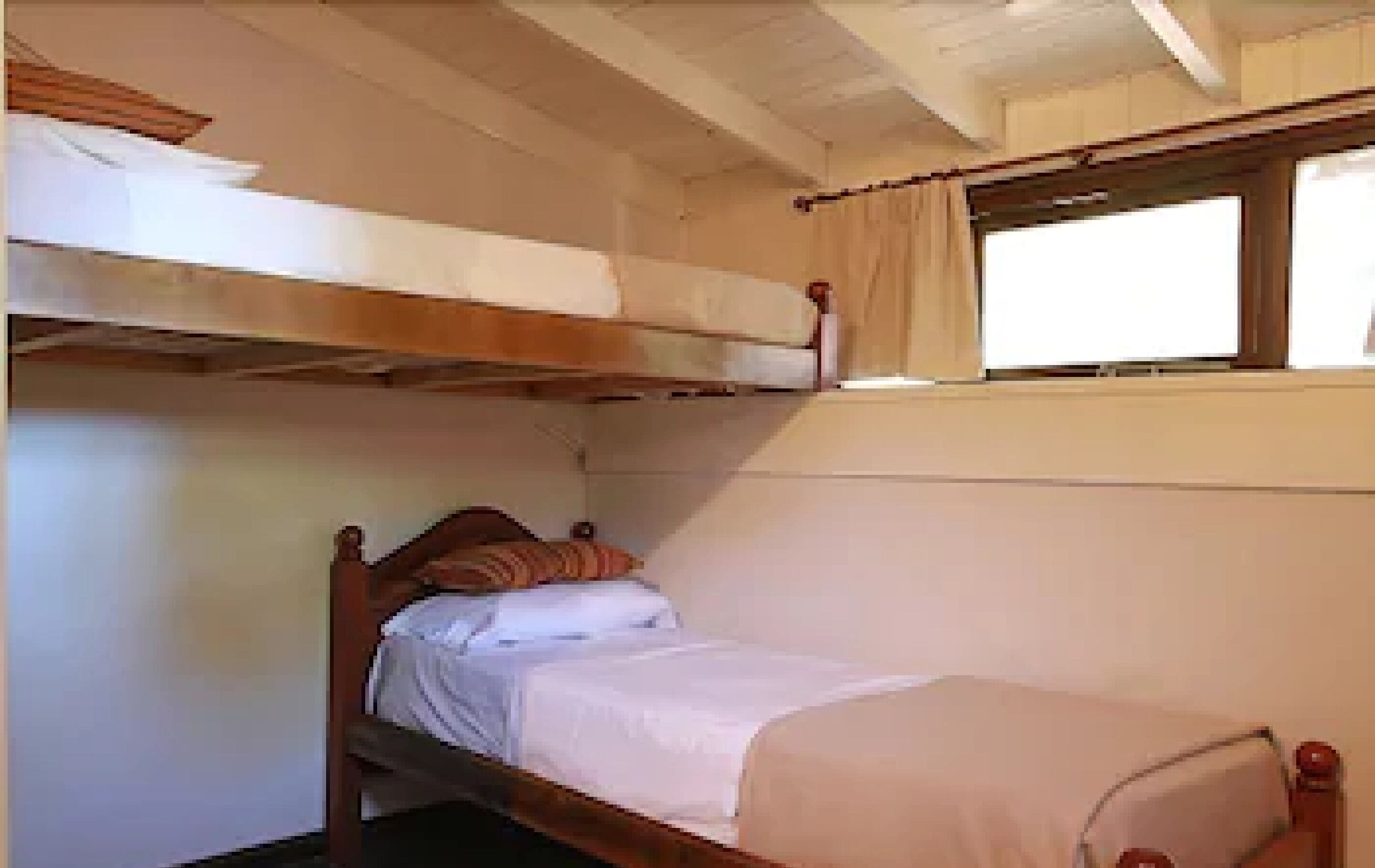 A bunk bed room with a window, wooden headboard, and a bedside table.