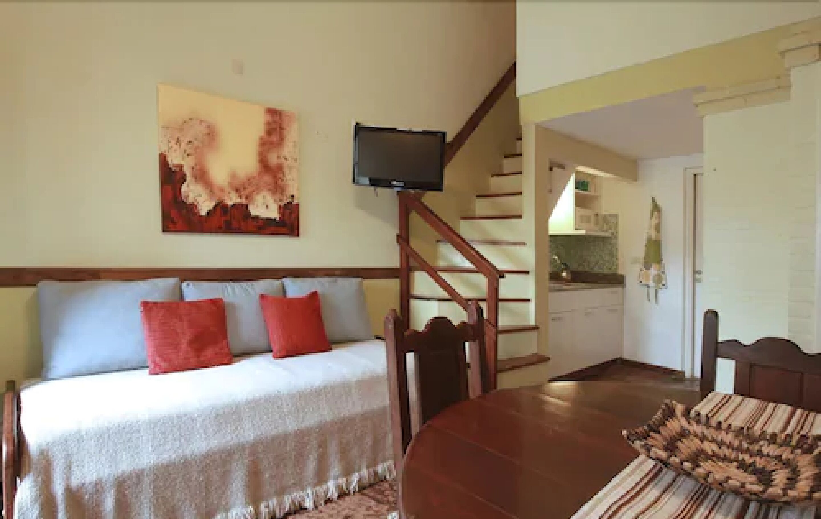 A bedroom with a bed, a television, a staircase, and a dining area.