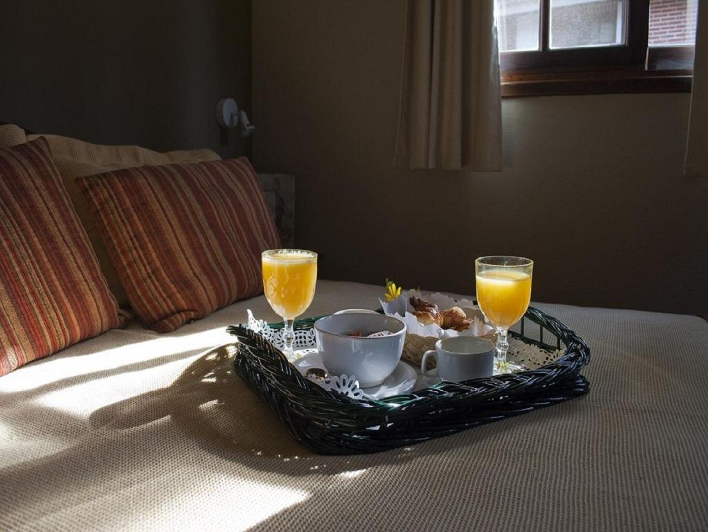 A breakfast tray on a bed with two glasses of orange juice, a cup of coffee, and a small bowl of cereal.