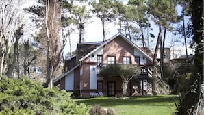 Ein zweigeschossiges Haus mit geneigtem Dach, umgeben von Bäumen und einem gepflegten Rasen.