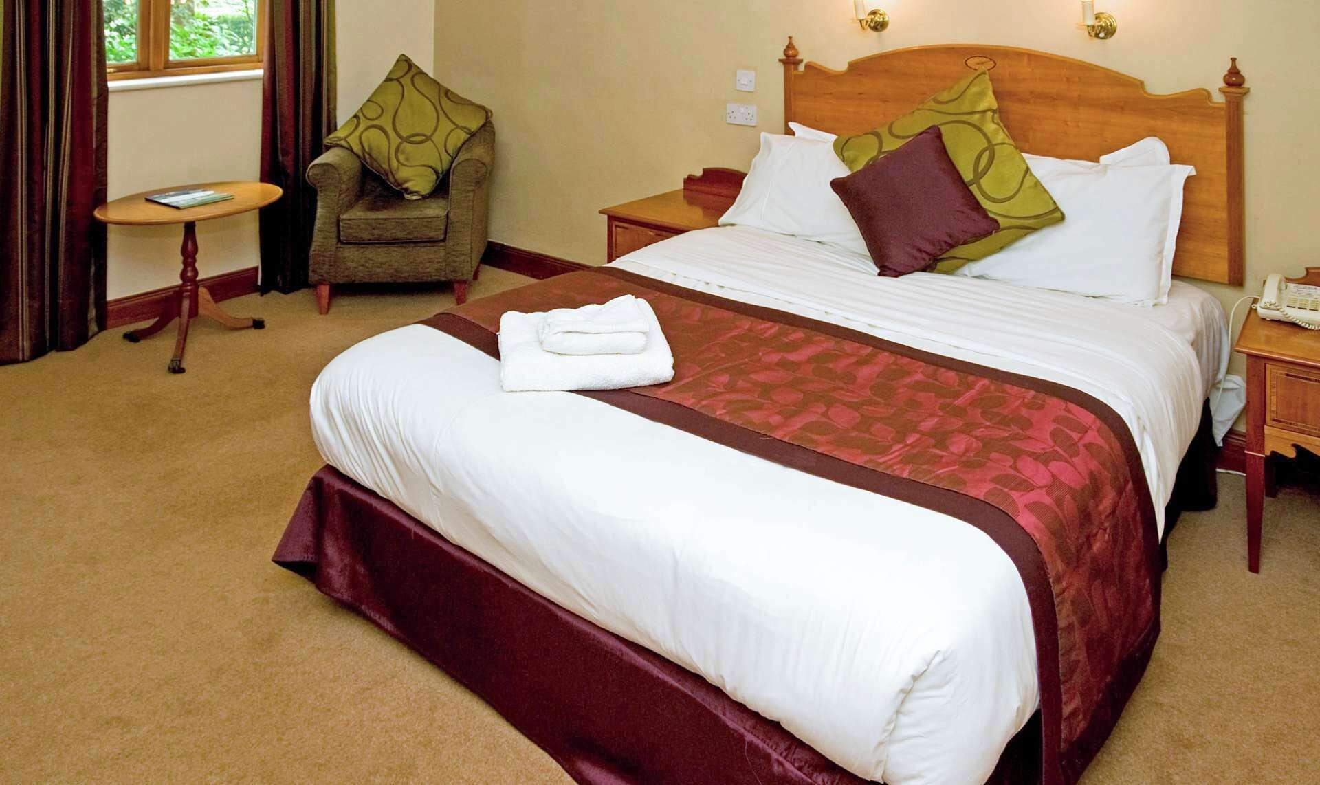 A neatly made bed with a white and maroon bedspread, a wooden headboard, and a bedside table with a telephone.