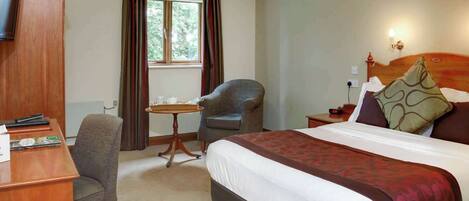 A hotel room with a bed, a desk with a chair, a small table, and a TV.