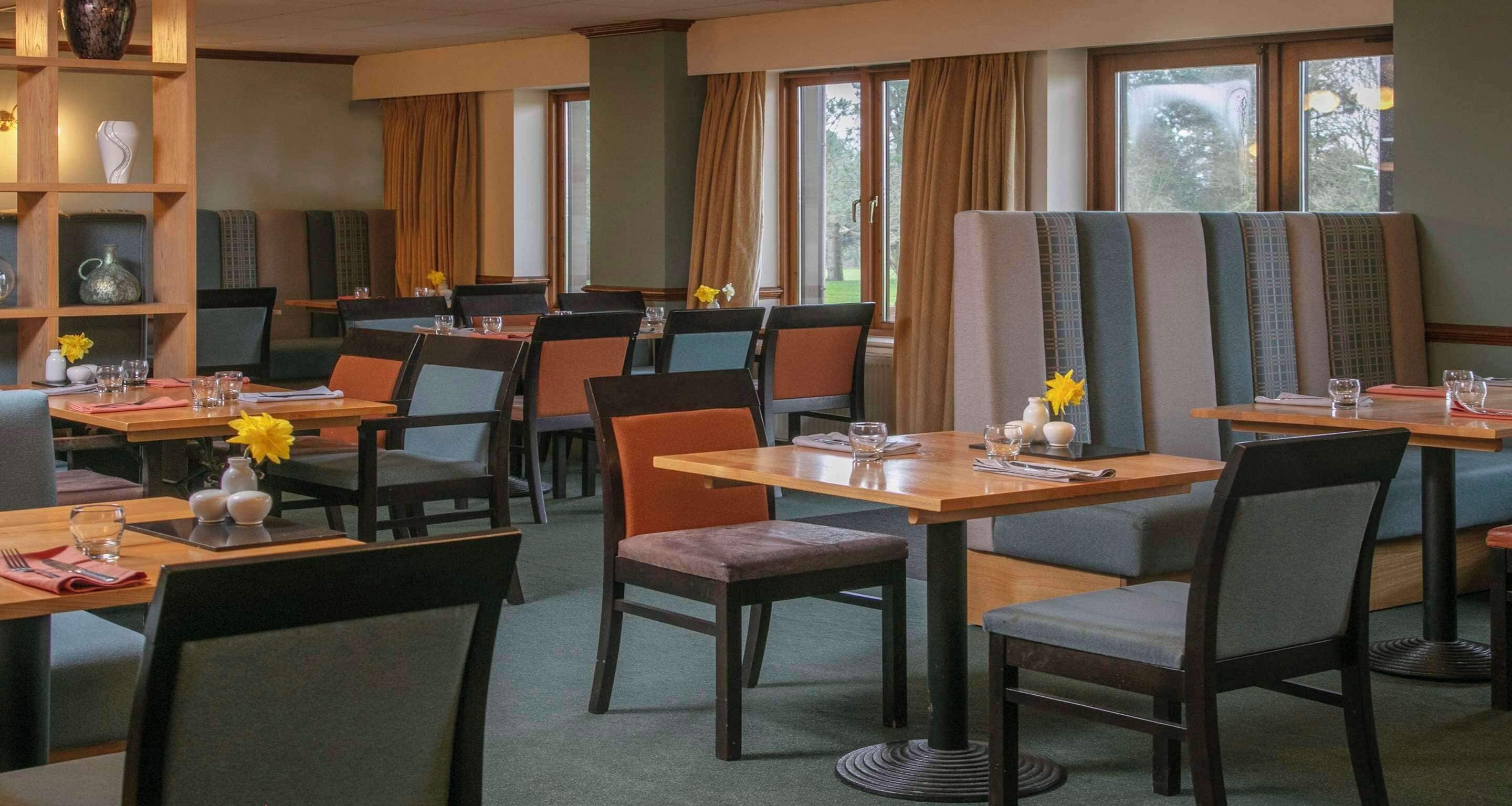 Un comedor de hotel con varias mesas y sillas, algunas con centros de mesa florales.
