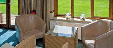 Habitación con vista a un campo de golf, que incluye un sofá, una mesa de vidrio y sillas de mimbre.
