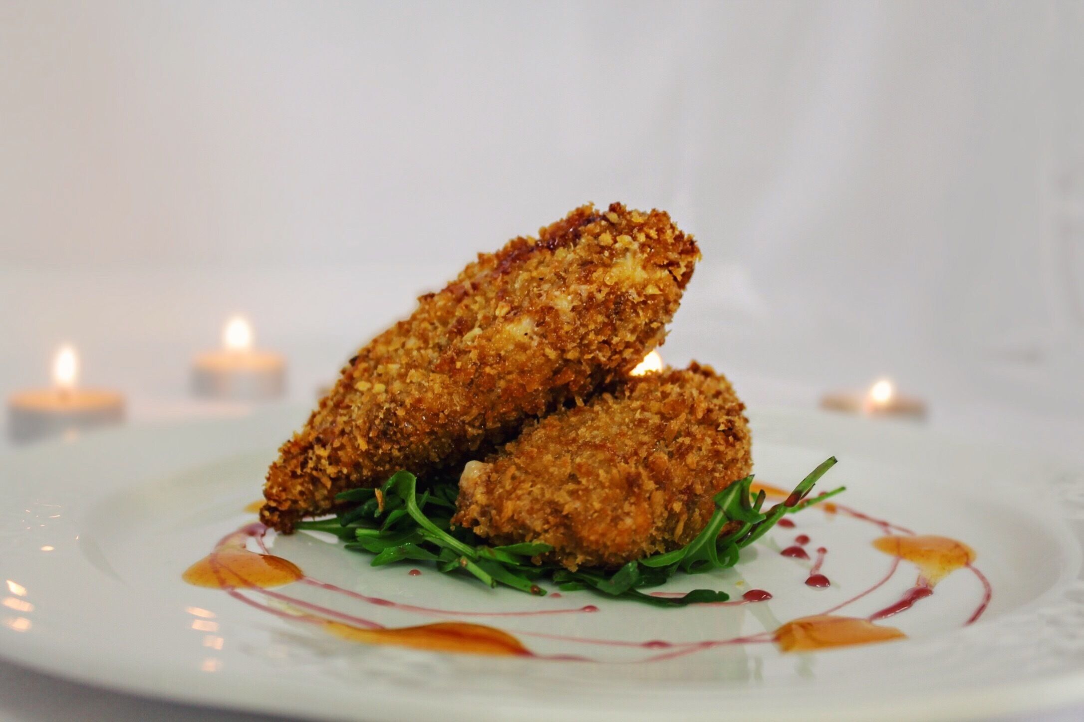 Um prato com dois alimentos empanados, guarnecido com vegetais e molho, sobre um prato branco com borda decorativa.