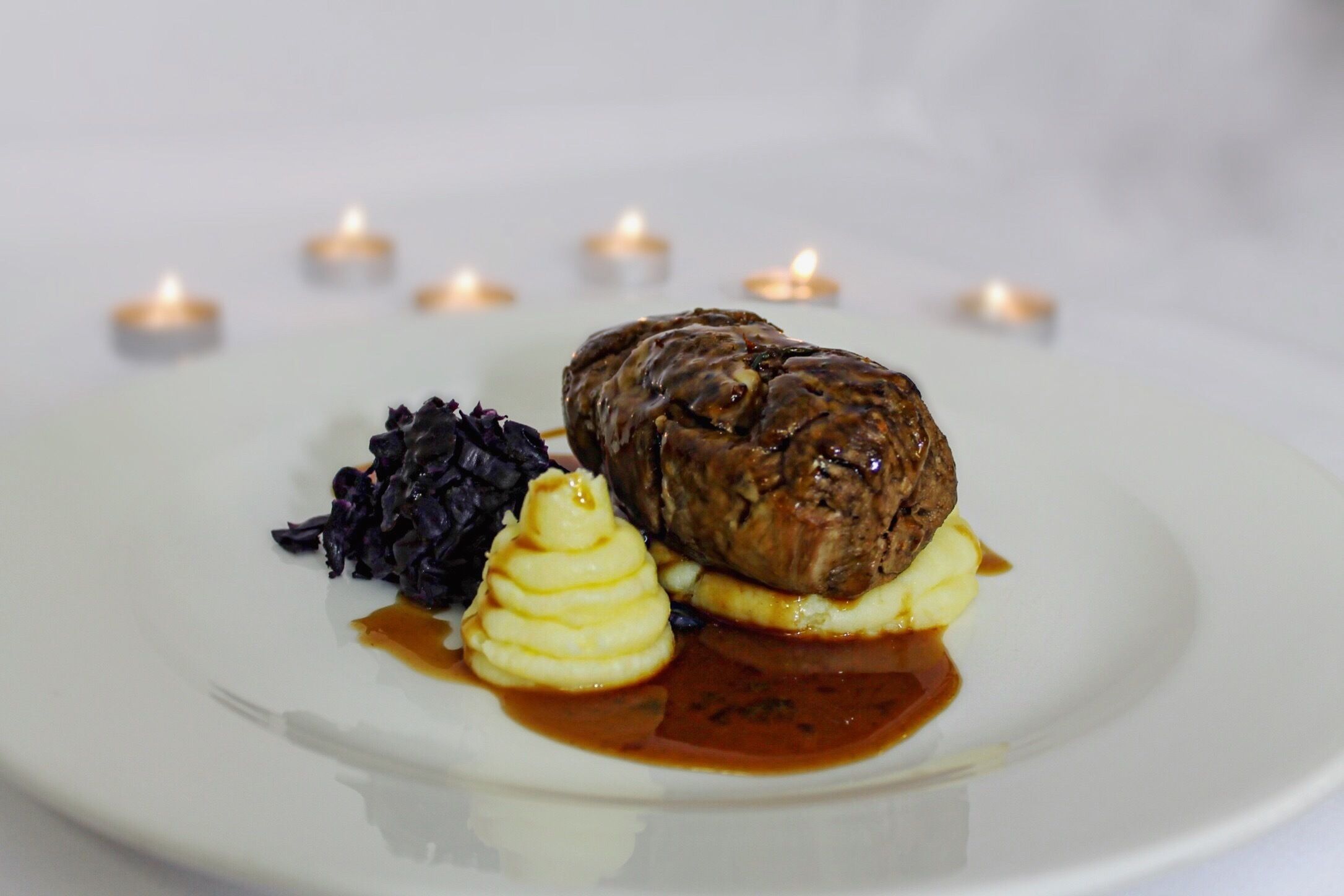 A plate with a meat dish, mashed potatoes, and a side of purple cabbage, accompanied by a sauce.