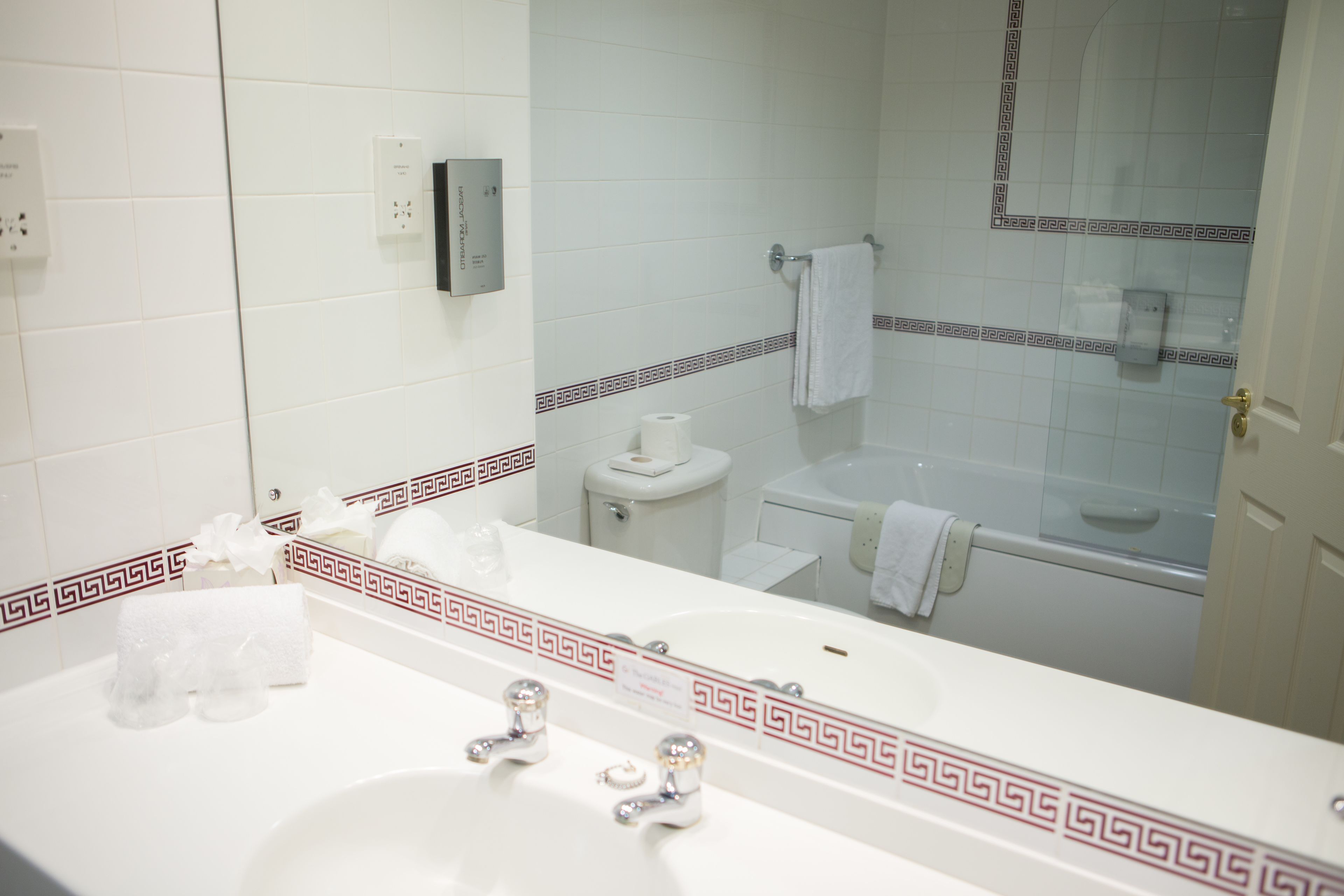 A bathroom with a white sink, two faucets, a mirror, a toilet, and a bathtub.