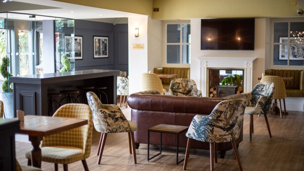 A modern interior with a brown leather sofa, patterned chairs, a wooden table, and a fireplace. - Best Western Bristol North The Gables Hotel (Wotton-under-Edge)