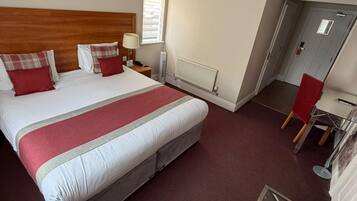 A hotel room with a large bed, a desk, a chair, a radiator, and a door.