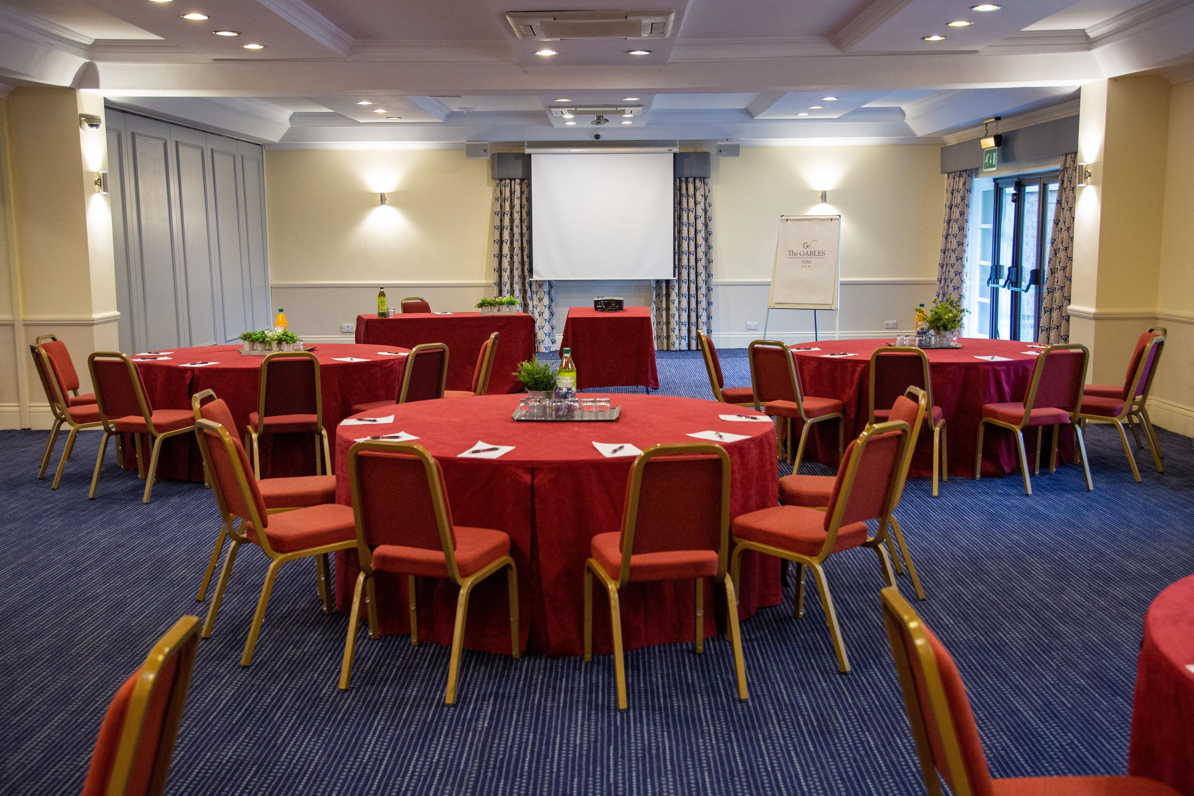 A conference room with round tables, chairs, and a projector screen.