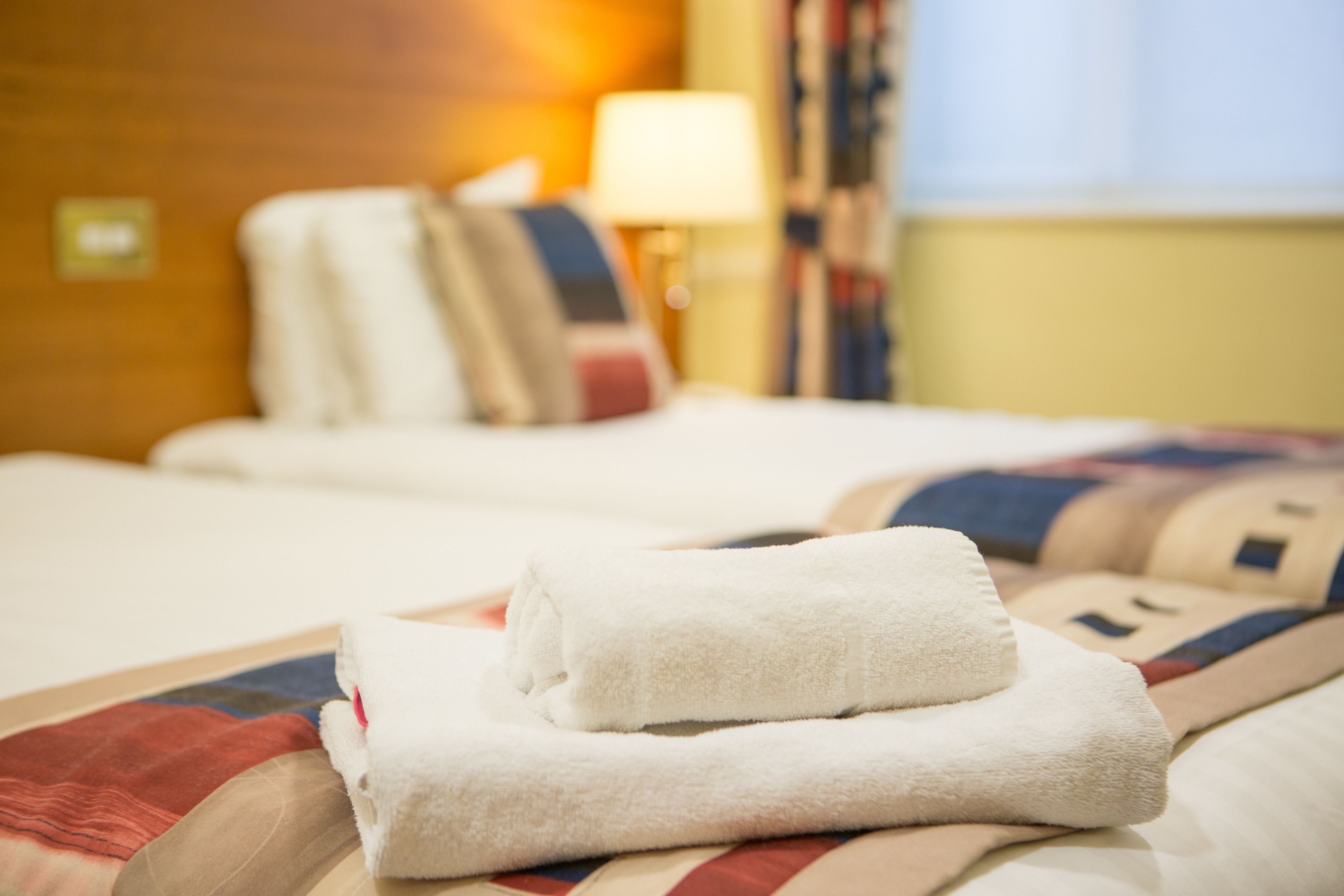 Una habitación de hotel con una cama bien tendida, una lámpara y una ventana con cortinas.