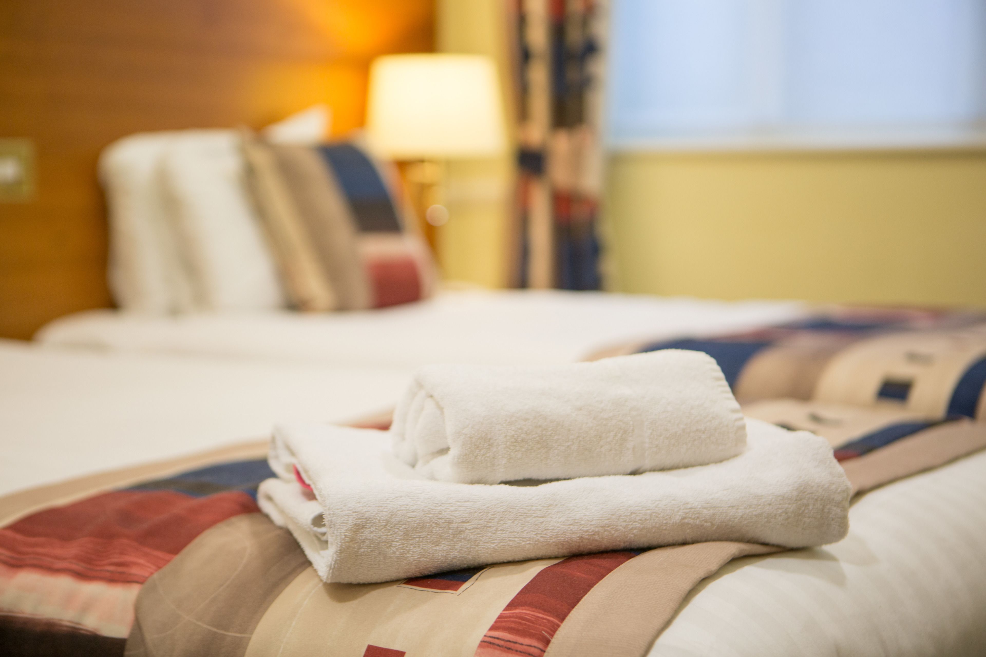 A neatly made bed with a folded white towel and a pillow.