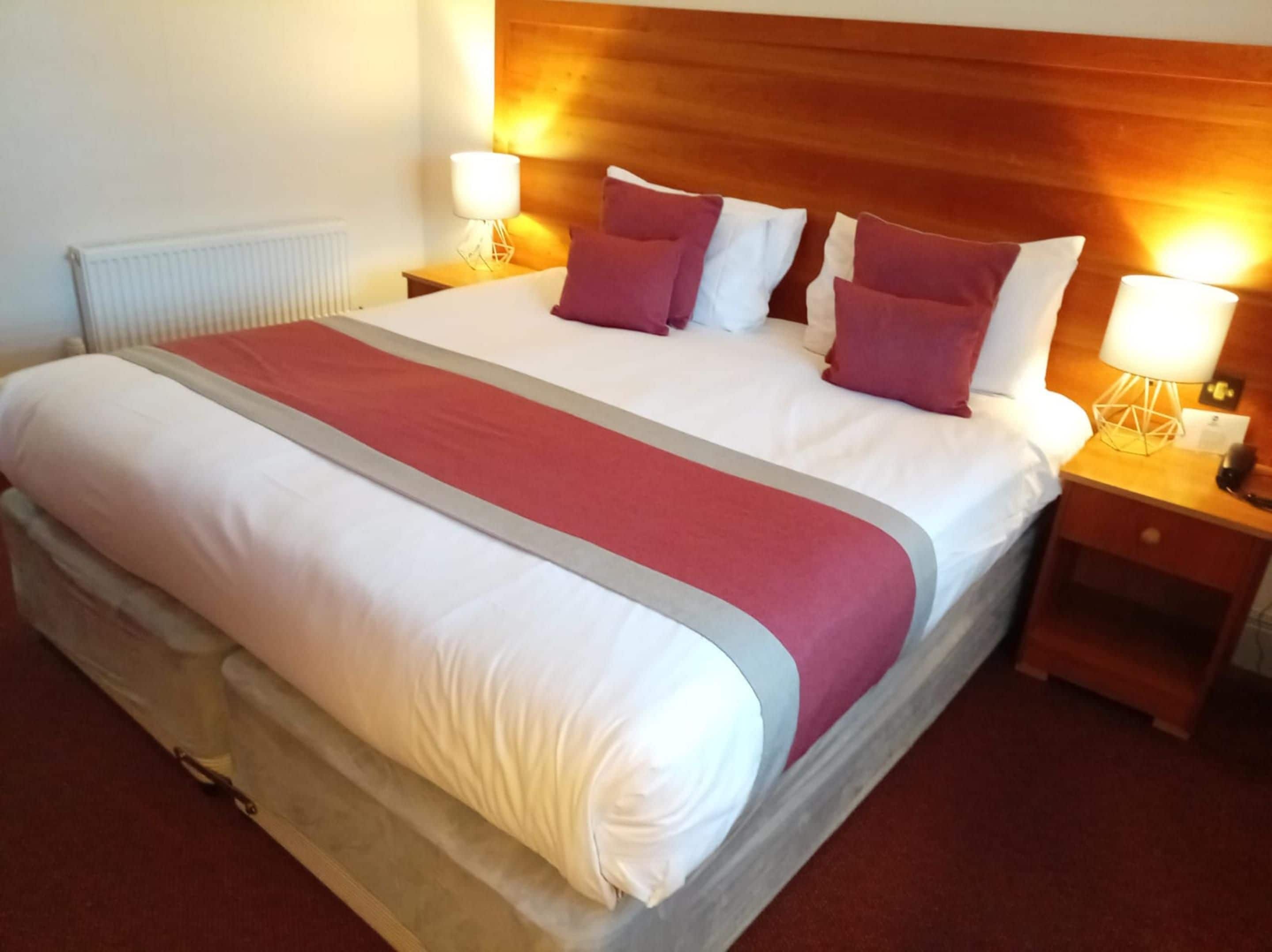 Une chambre d’hôtel avec un grand lit, deux tables de chevet avec des lampes et une tête de lit en bois.