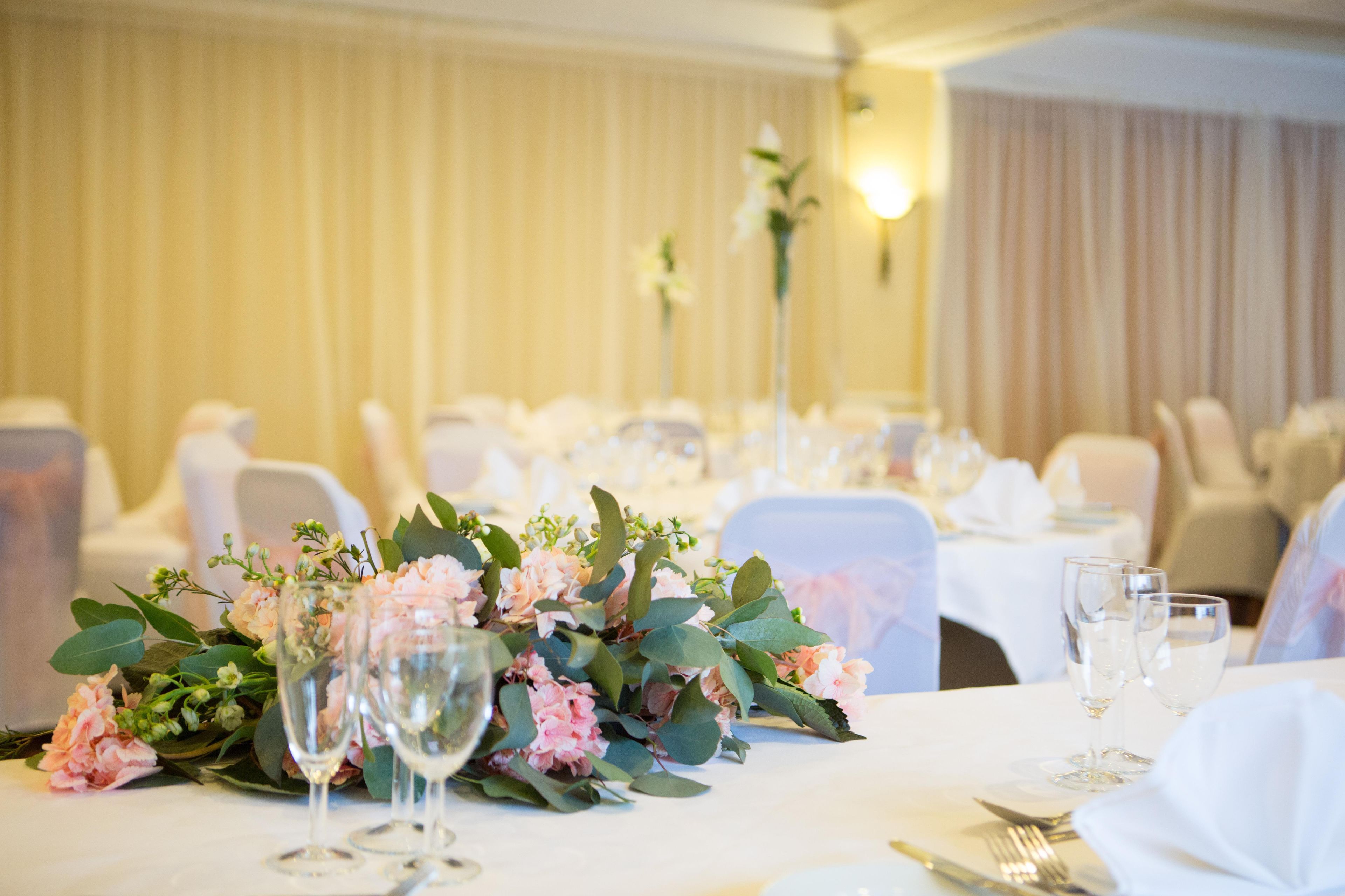 A banquet table set with glassware, plates, and a centerpiece of flowers.