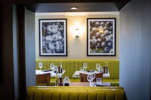 Un restaurante con asientos y mesas verdes, cada conjunto con copas y botellas de vino.