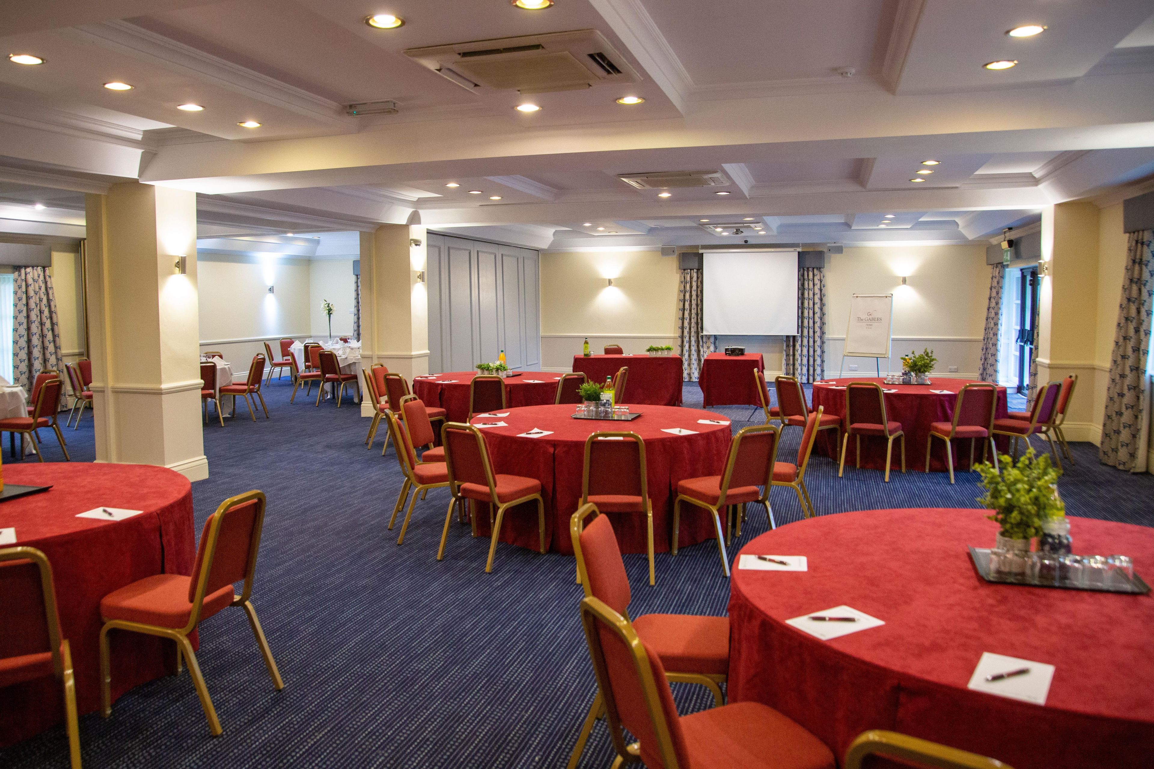 A conference room with multiple round tables and chairs, equipped with nameplates and pens.