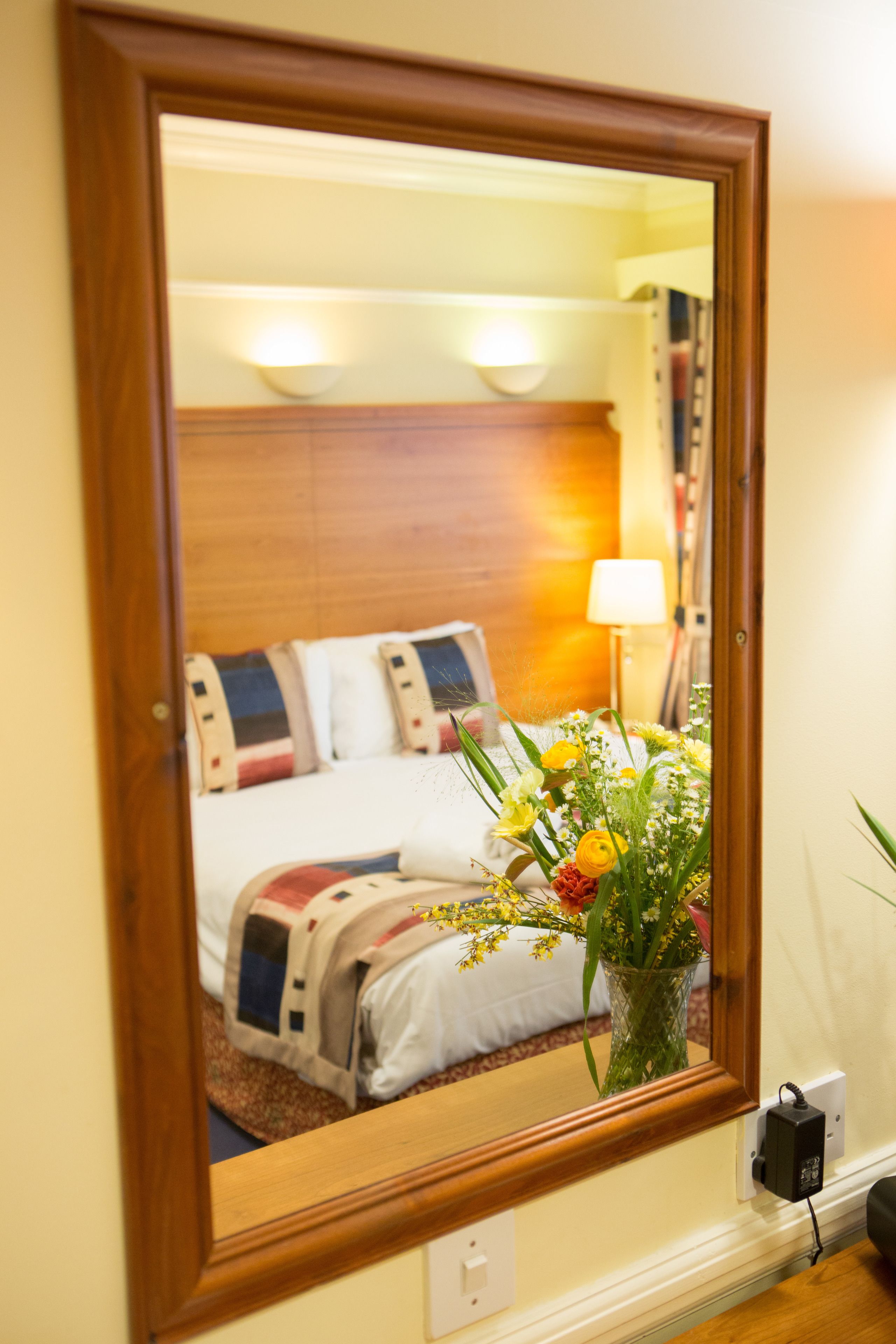 Una habitació d'hotel amb un panell de fusta al capçal del llit, un llit amb un edredó de motius florals i un ram de flors a la tauleta de nit.