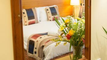 Una habitació d'hotel amb un panell de fusta al capçal del llit, un llit amb un edredó de motius florals i un ram de flors a la tauleta de nit.