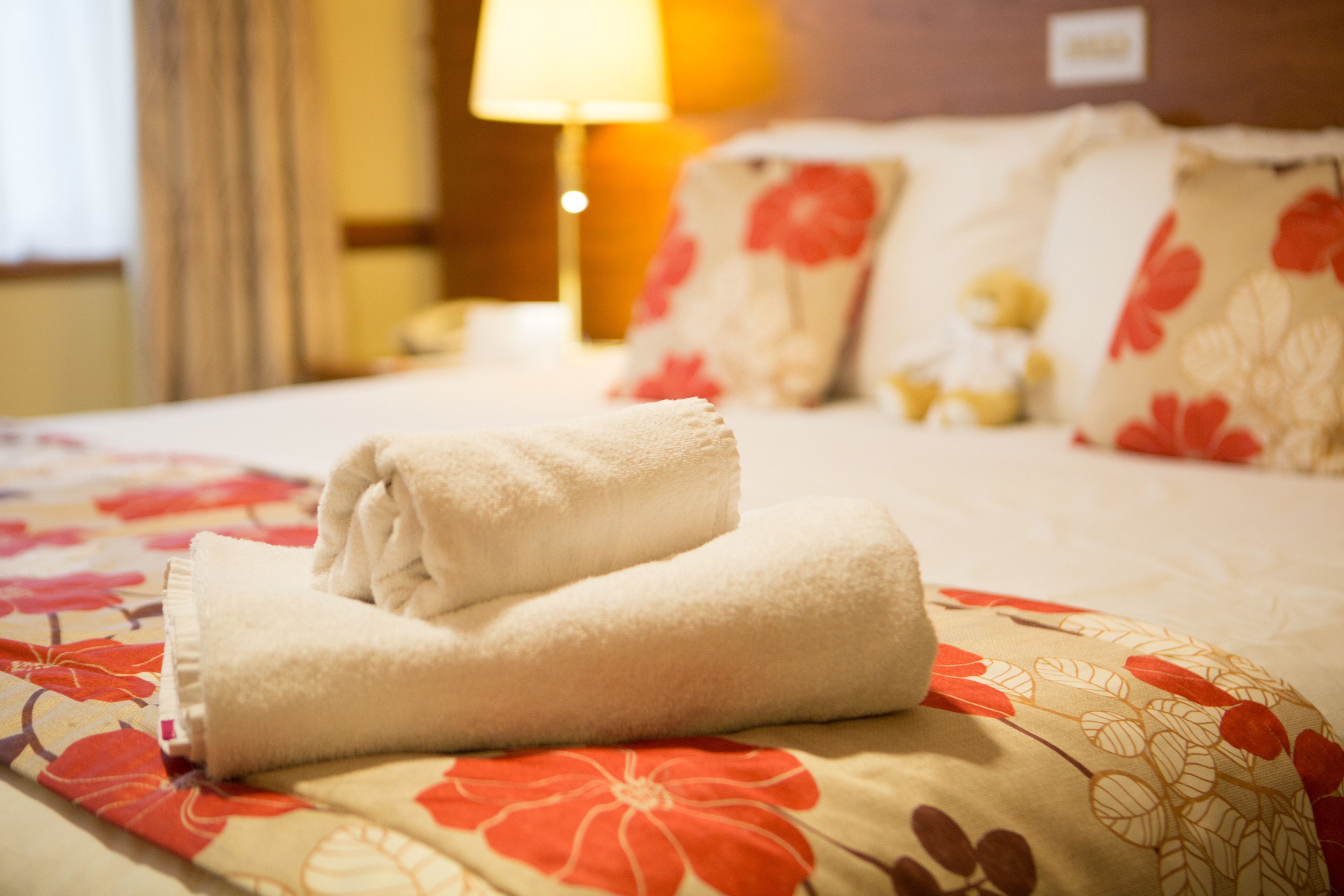 Una cama bien hecha con una colcha de estampado floral y una toalla blanca doblada.