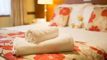 Una cama bien hecha con una colcha de estampado floral y una toalla blanca doblada.