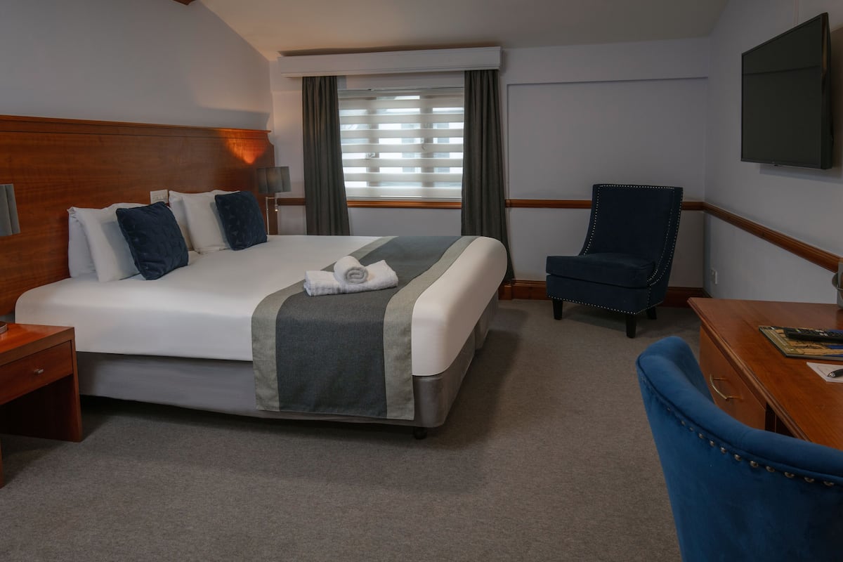 Habitación de hotel con una cama grande, un escritorio, una silla y un televisor montado en la pared.