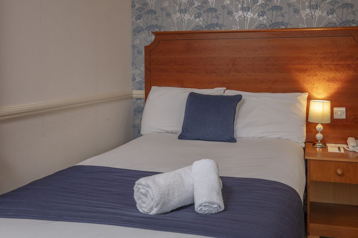 Una cama bien hecha con una colcha azul y blanca, cabecera de madera y una lámpara de noche.