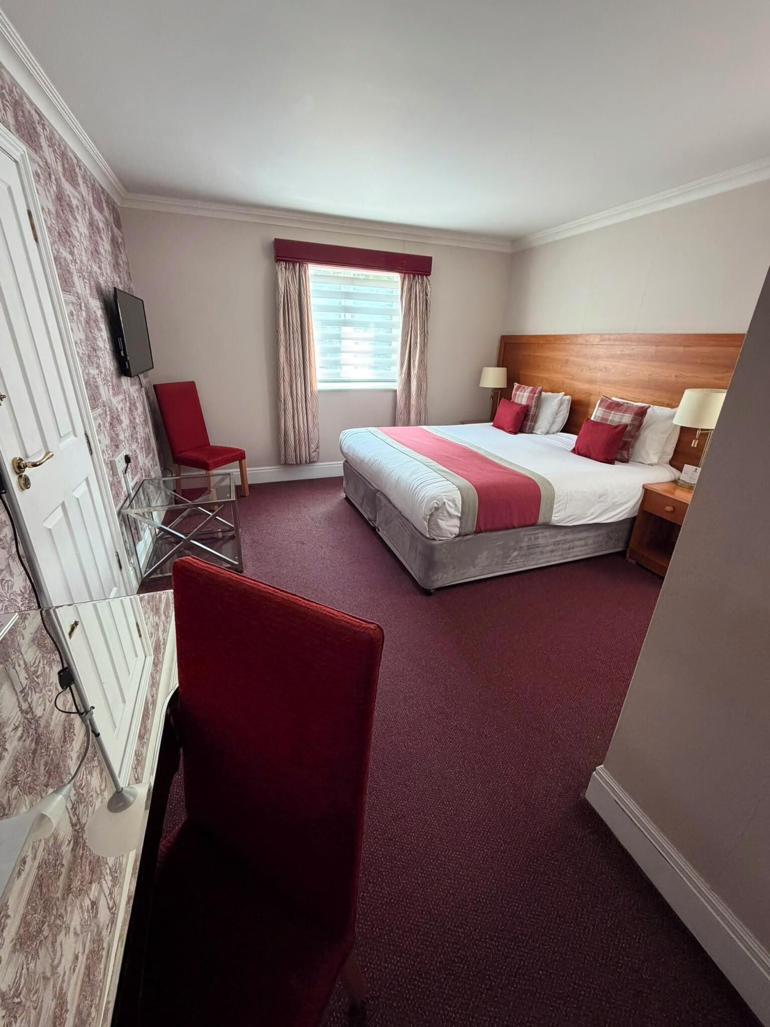 Een hotelkamer met een bed, een bureau, een stoel, een televisie en een raam met gordijnen.